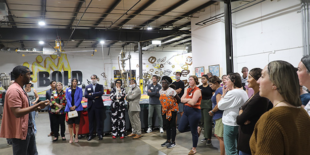 A group of people standing in a factory listening to a man speak.
